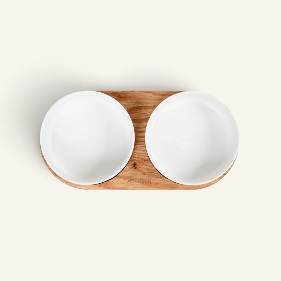 Patomia Barcelona double dog bowl with a light oiled oak wooden base and two white ceramic bowls, top view.