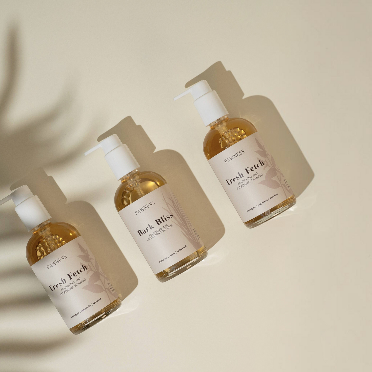 Patomia Bark Bliss and Fresh Fetch natural dog shampoos in clear pump bottles on a beige background with leaf shadows.