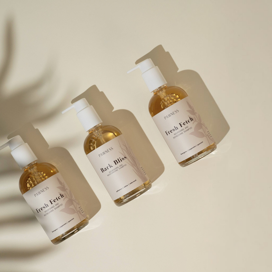Patomia Bark Bliss and Fresh Fetch natural dog shampoos in clear pump bottles on a beige background with leaf shadows.