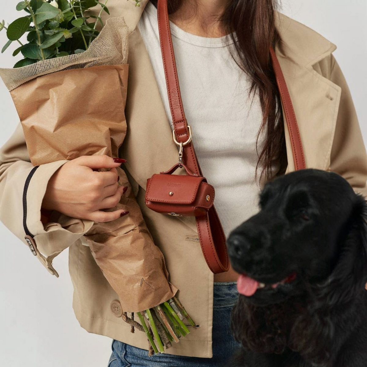 Patomia brown vegan leather dog leash with matching waste bag holder worn over the shoulder by a woman with a dog