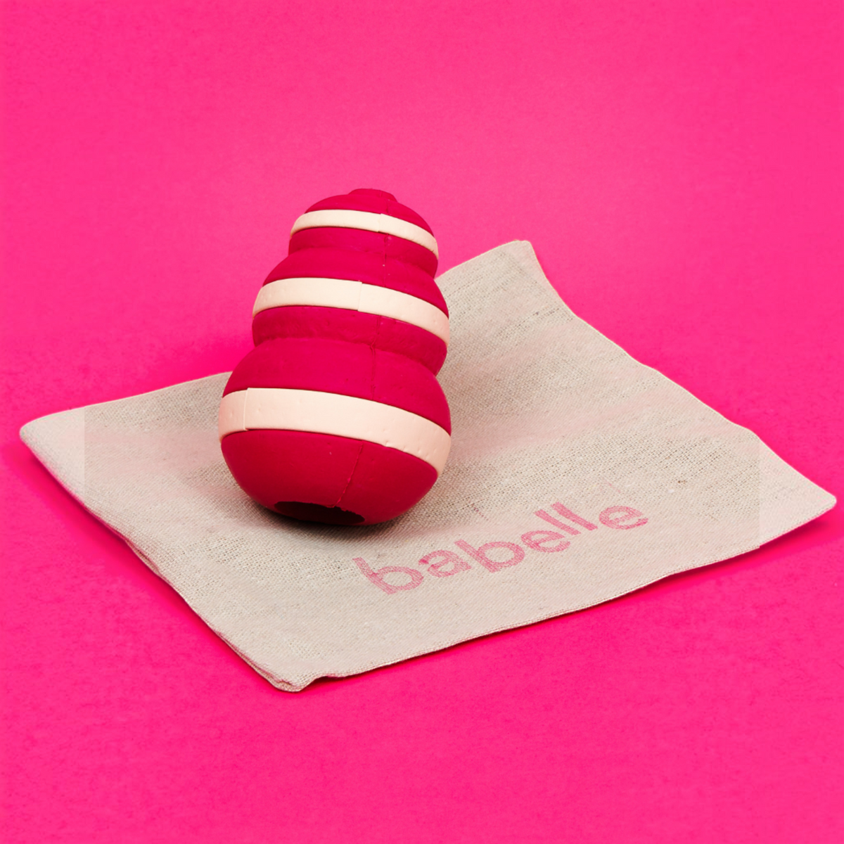 Patomia Bubble dog treat dispenser toy in red and cream silicone on a small fabric bag against a bright pink background
