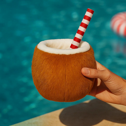Patomia soft plush coconut dog toy with a red and white striped straw, held by a hand near a swimming pool.