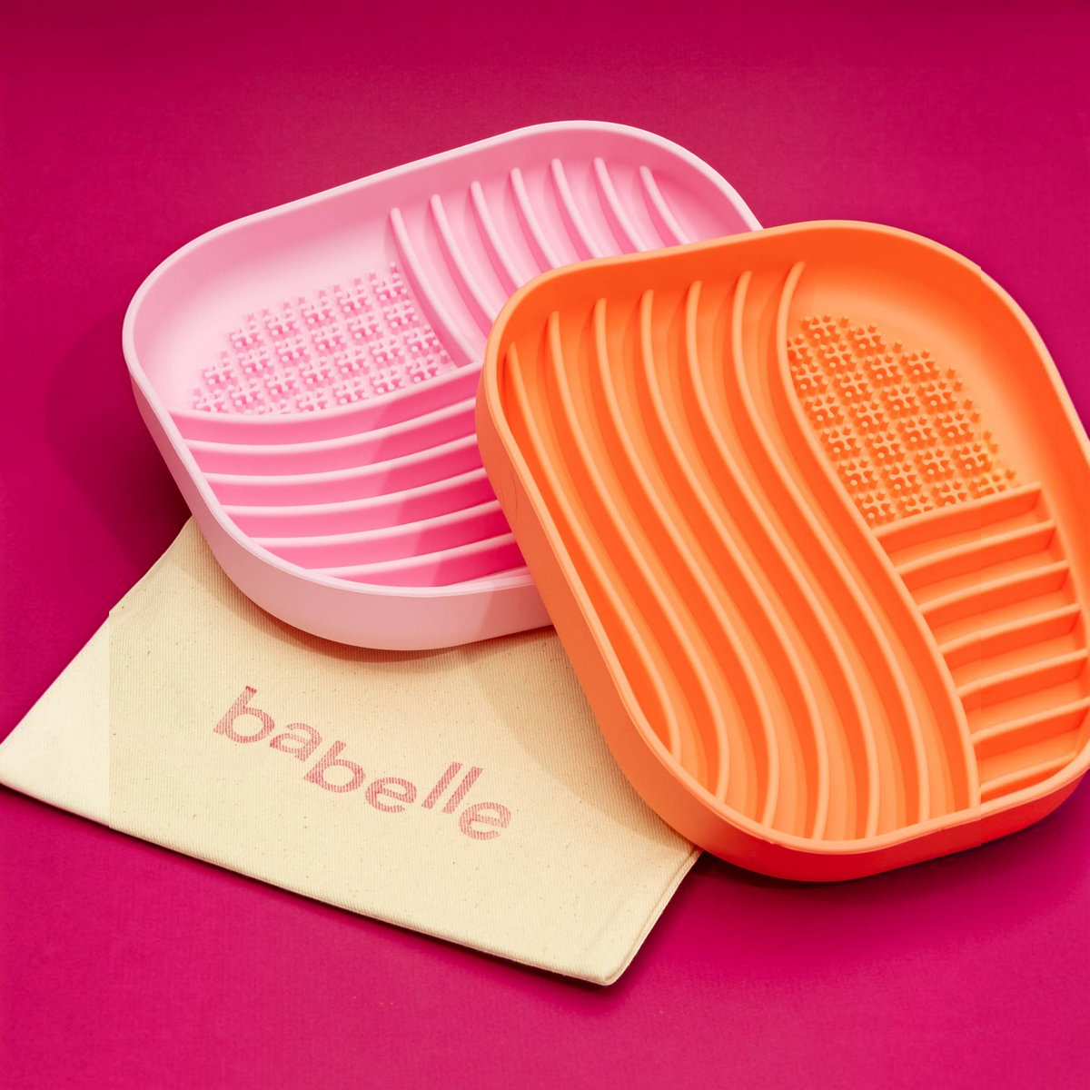 Patomia coral and pink silicone slow feeder lick mats with textured wavy surfaces for dogs on a magenta background.