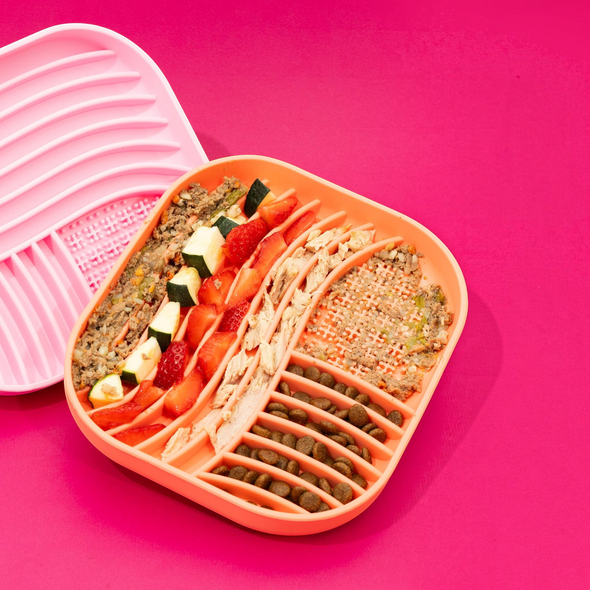 Patomia coral silicone lick mat with textured wavy surface filled with healthy pet food on a bright pink background
