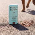 Charger l'image dans la visionneuse de la galerie, Patomia dog paw balm stick in light blue packaging on hot asphalt with a paw print mark, protecting pet skin.
