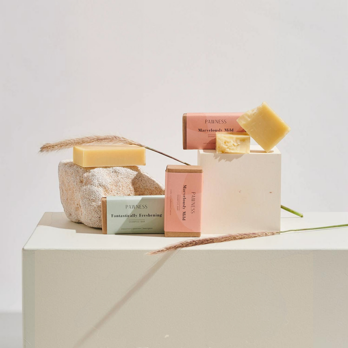 Patomia dog shampoo bars in eco-friendly packaging with natural soap blocks displayed on stone and wooden pedestals.
