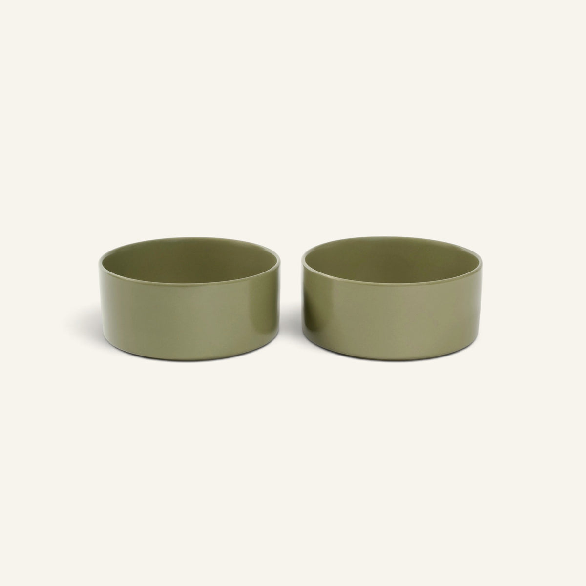 Two olive green Patomia ceramic dog bowls with a minimalist design and smooth finish on a light background