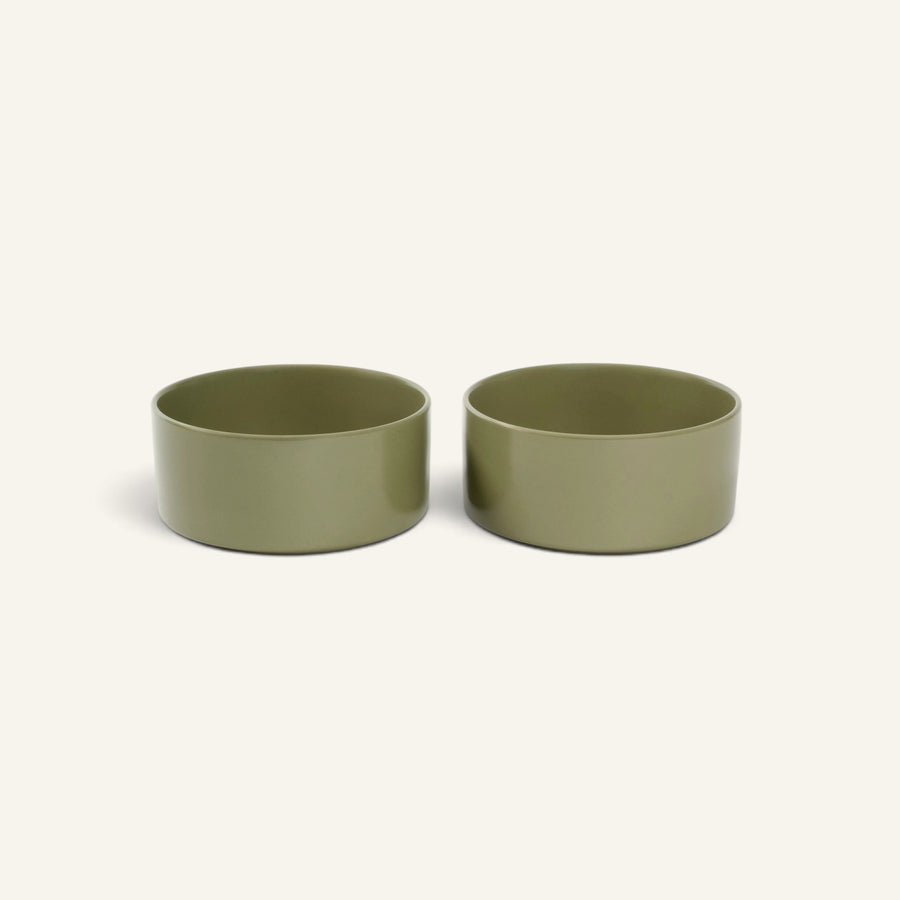 Two olive green Patomia ceramic dog bowls with a minimalist design and smooth finish on a light background