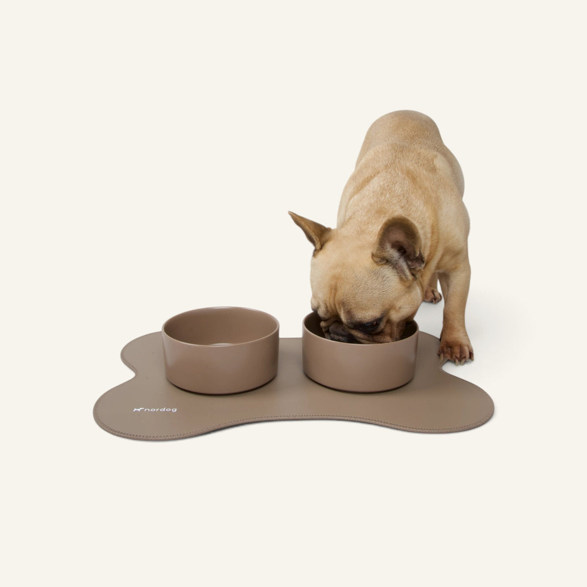Patomia Nordog ceramic dog bowl set in cacao brown on a matching bone-shaped mat with a French Bulldog eating