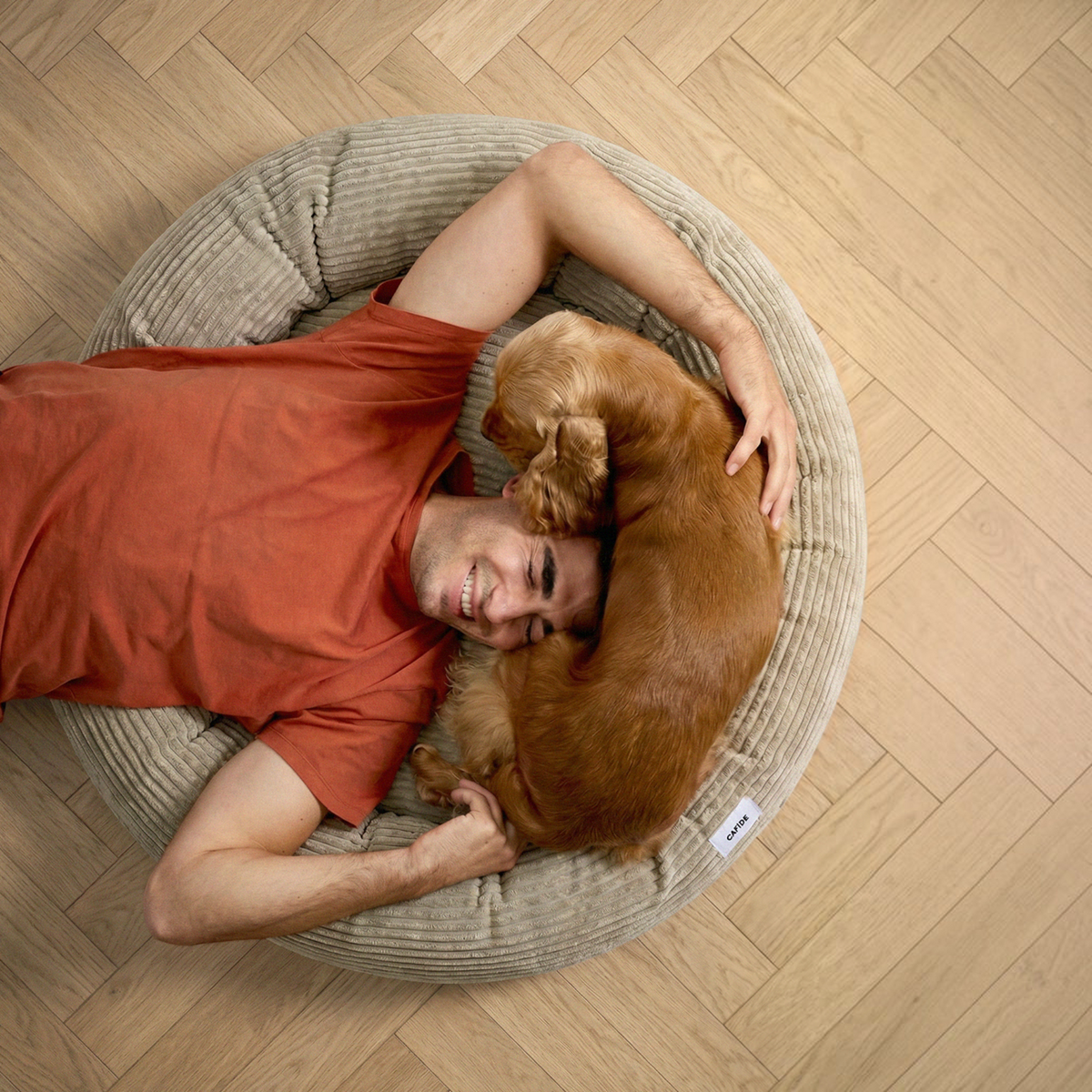Patomia Nuba beige corduroy dog bed with a man and a golden spaniel dog lying together on a wooden floor