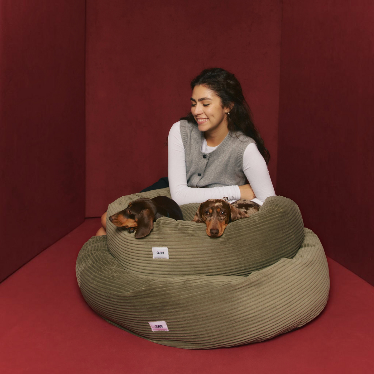 Patomia Nuba green corduroy dog bed with two dachshunds, featuring a woman sitting behind the plush pet cushions.