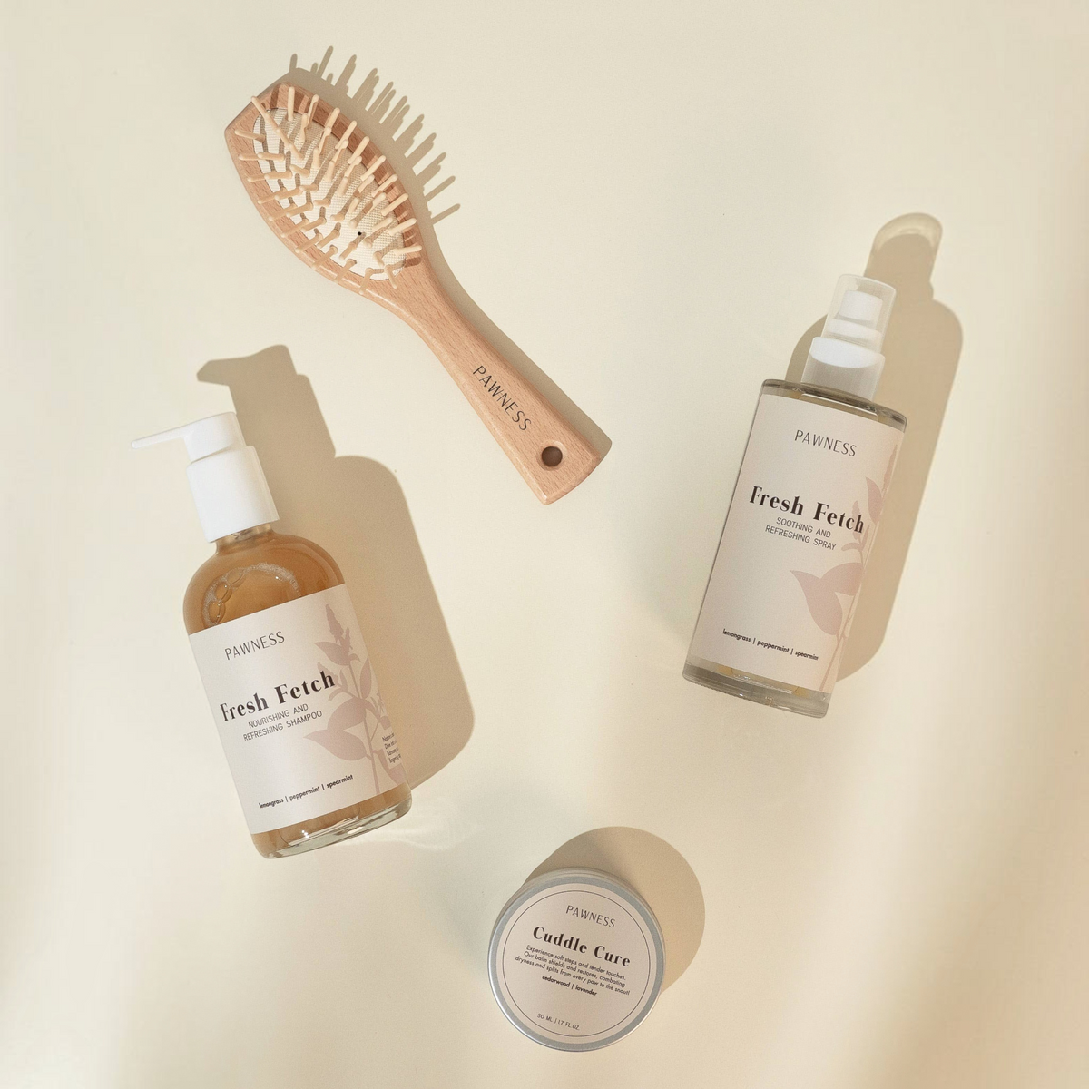 Patomia Pawness dog grooming set with Fresh Fetch spray, shampoo, wooden brush, and Cuddle Cure balm on beige surface