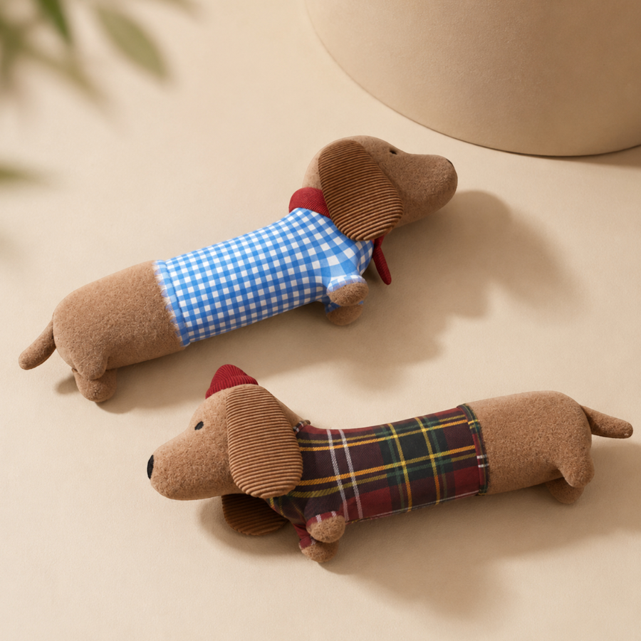 Two Patomia plush dachshund dog toys with squeakers, wearing blue gingham and red plaid outfits on a beige background.
