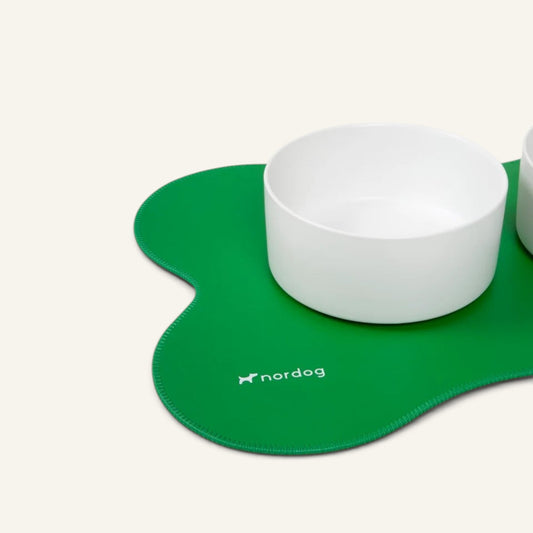 Patomia white ceramic dog bowl by Nordog resting on a green clover-shaped non-slip mat